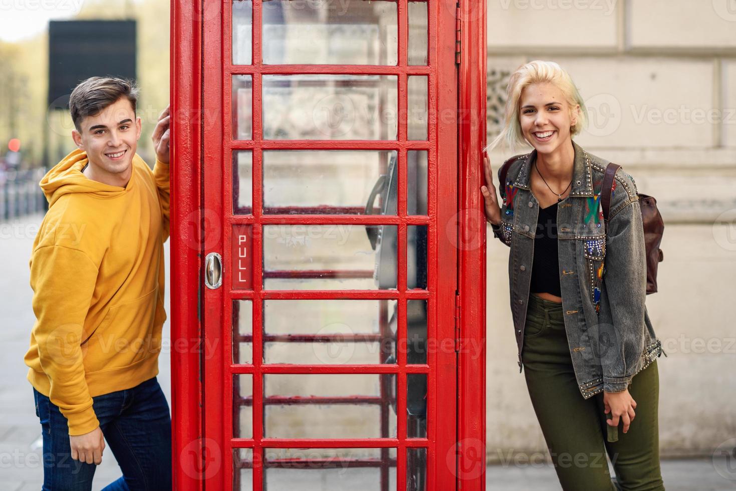 jovem casal de amigos perto de uma cabine telefônica vermelha britânica clássica foto