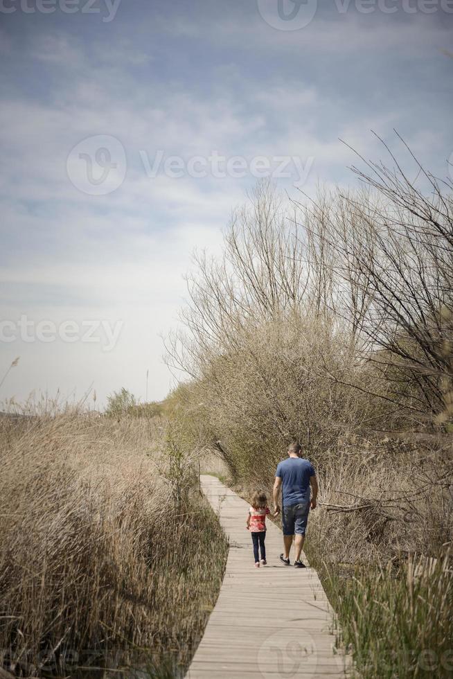 pai e filha caminhando por um caminho de tábuas de madeira em um pântano foto