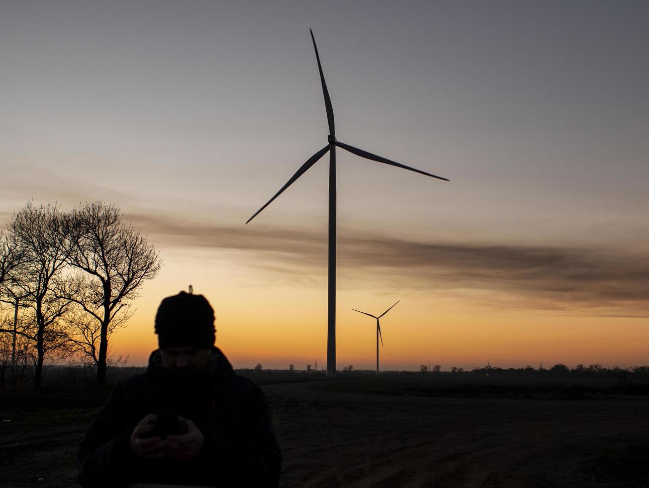 silhueta de um homem ao pôr do sol tirando uma foto das turbinas eólicas. usinas de energia do vento ao pôr do sol