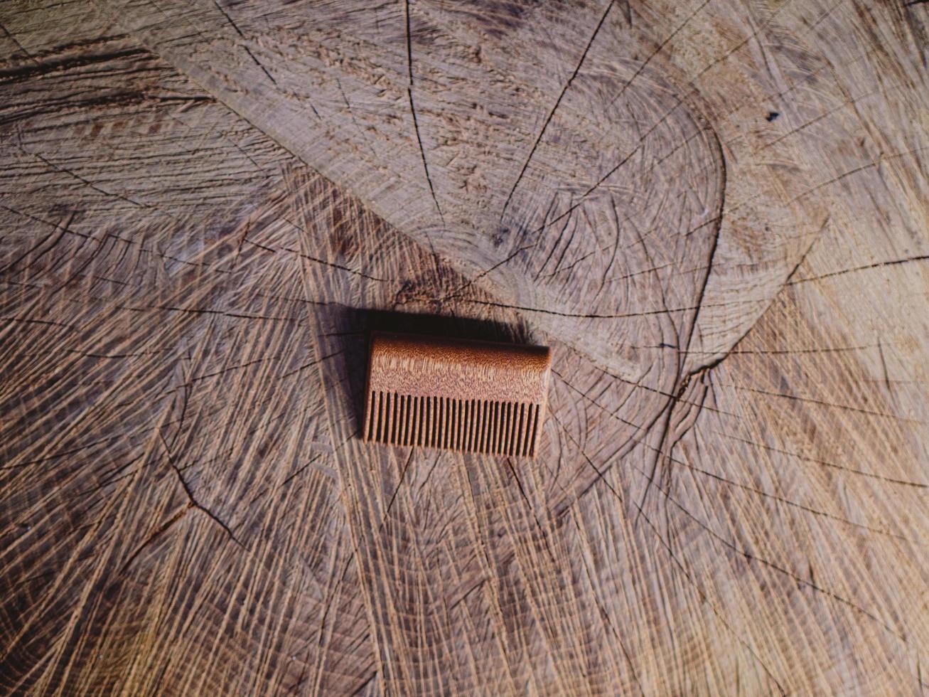 pente de barba feito à mão em um toco de madeira. conceito de barba e bigode. acessórios para barba. pente de barba de madeira foto