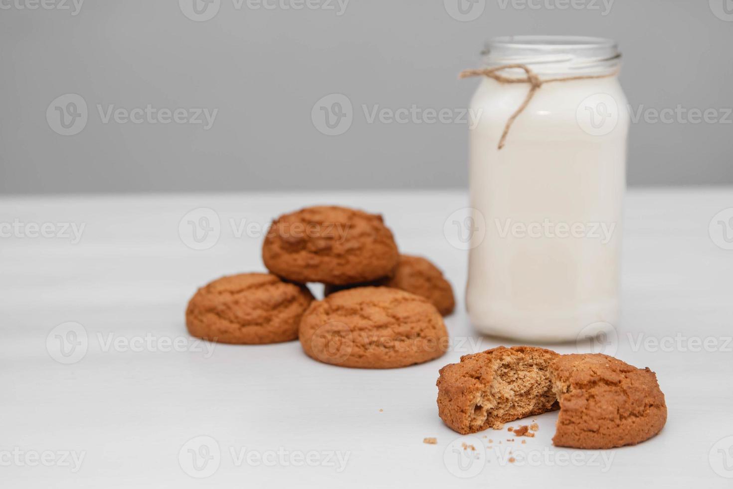 leite em uma jarra de vidro e biscoitos de aveia em uma mesa branca foto