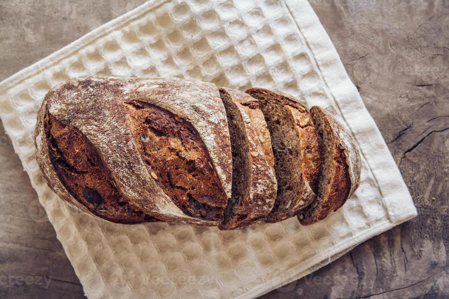 pão fresco marrom com sementes são cortados em pedaços em um fundo de madeira velha foto