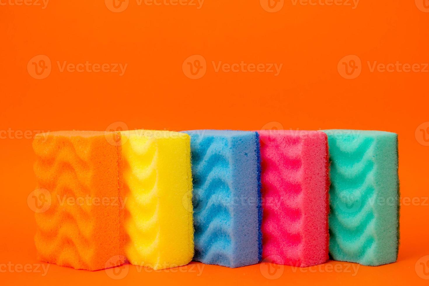 esponjas multicoloridas para limpar e lavar pratos em um fundo laranja foto