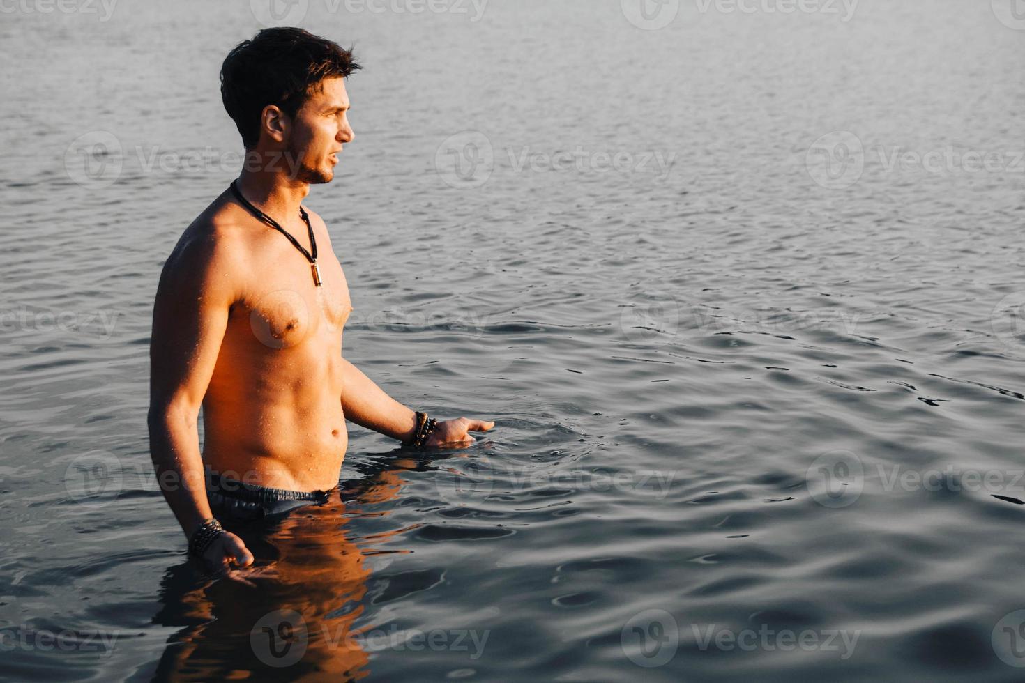 homem com arquibancadas musculares perfeitas na água ao pôr do sol foto