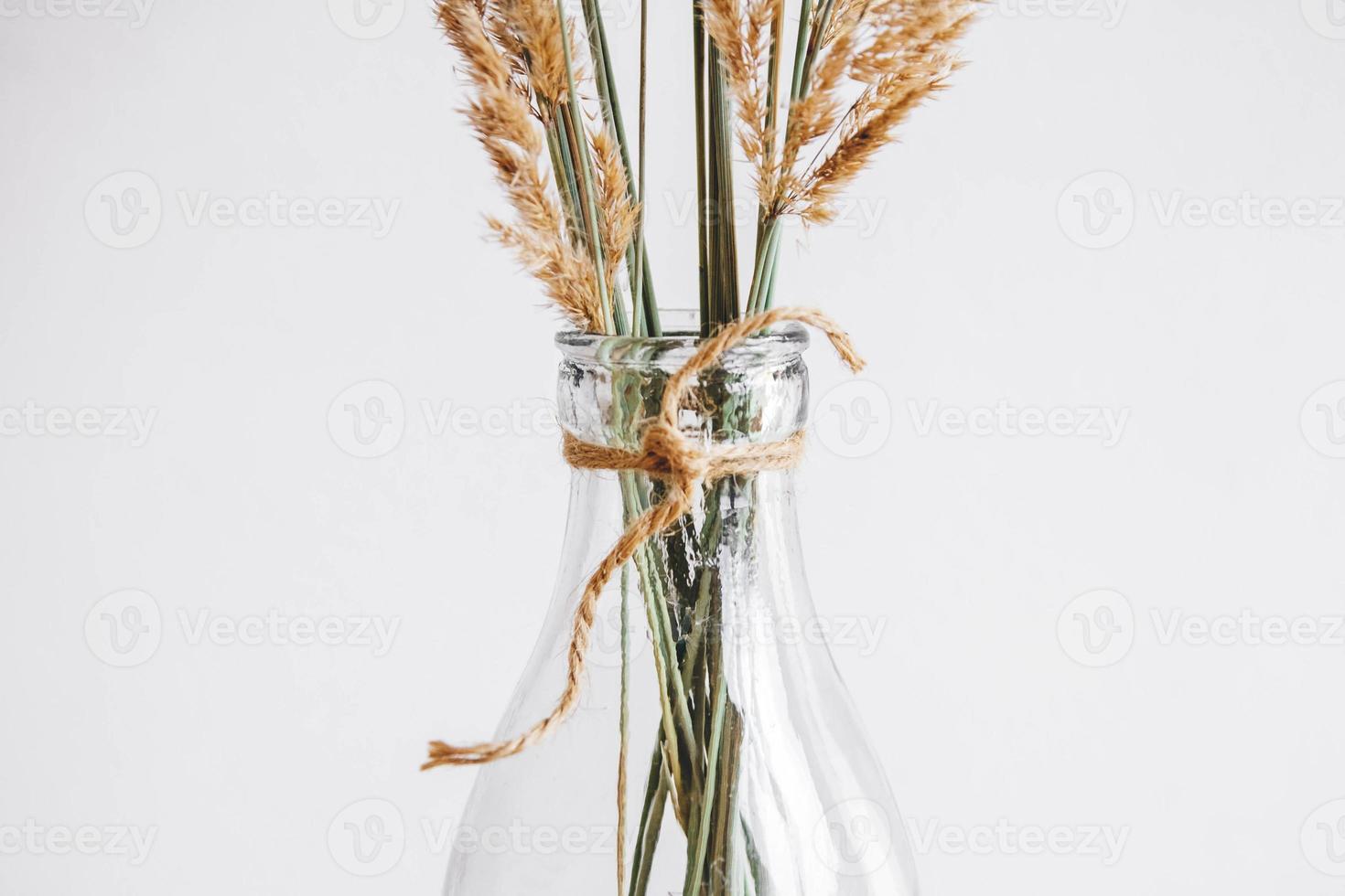 natureza morta de um buquê de flores secas em uma garrafa de vidro sobre uma mesa de madeira foto