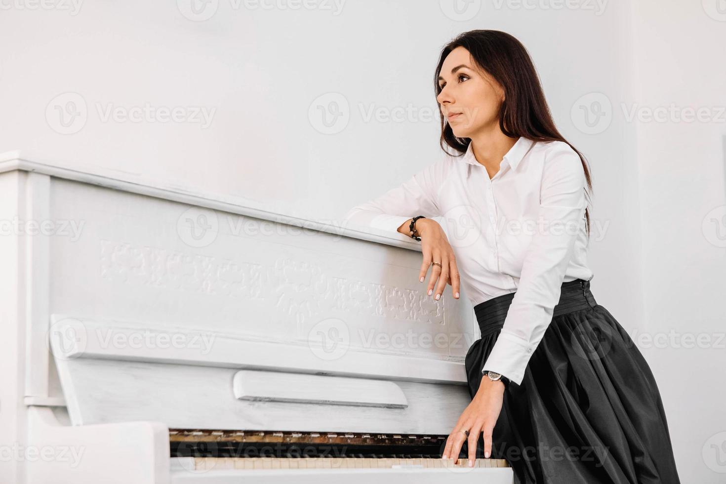 linda mulher vestida de camisa branca, tocando piano branco. lugar para texto ou publicidade foto