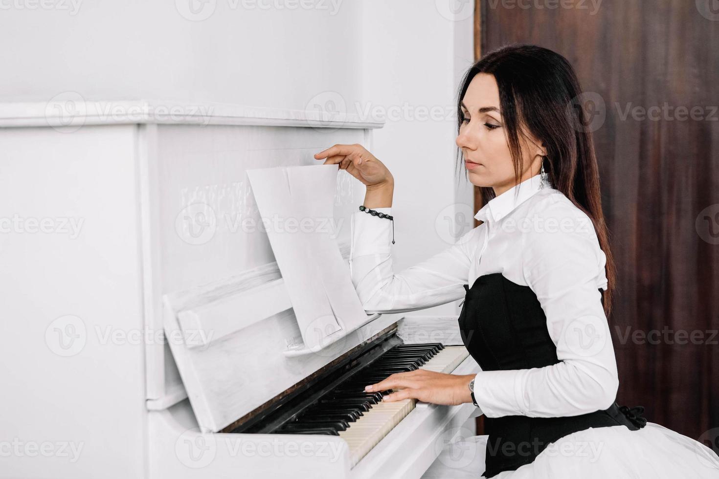 linda mulher vestida de camisa branca olha para as notas musicais e tocando piano branco. lugar para texto ou publicidade foto