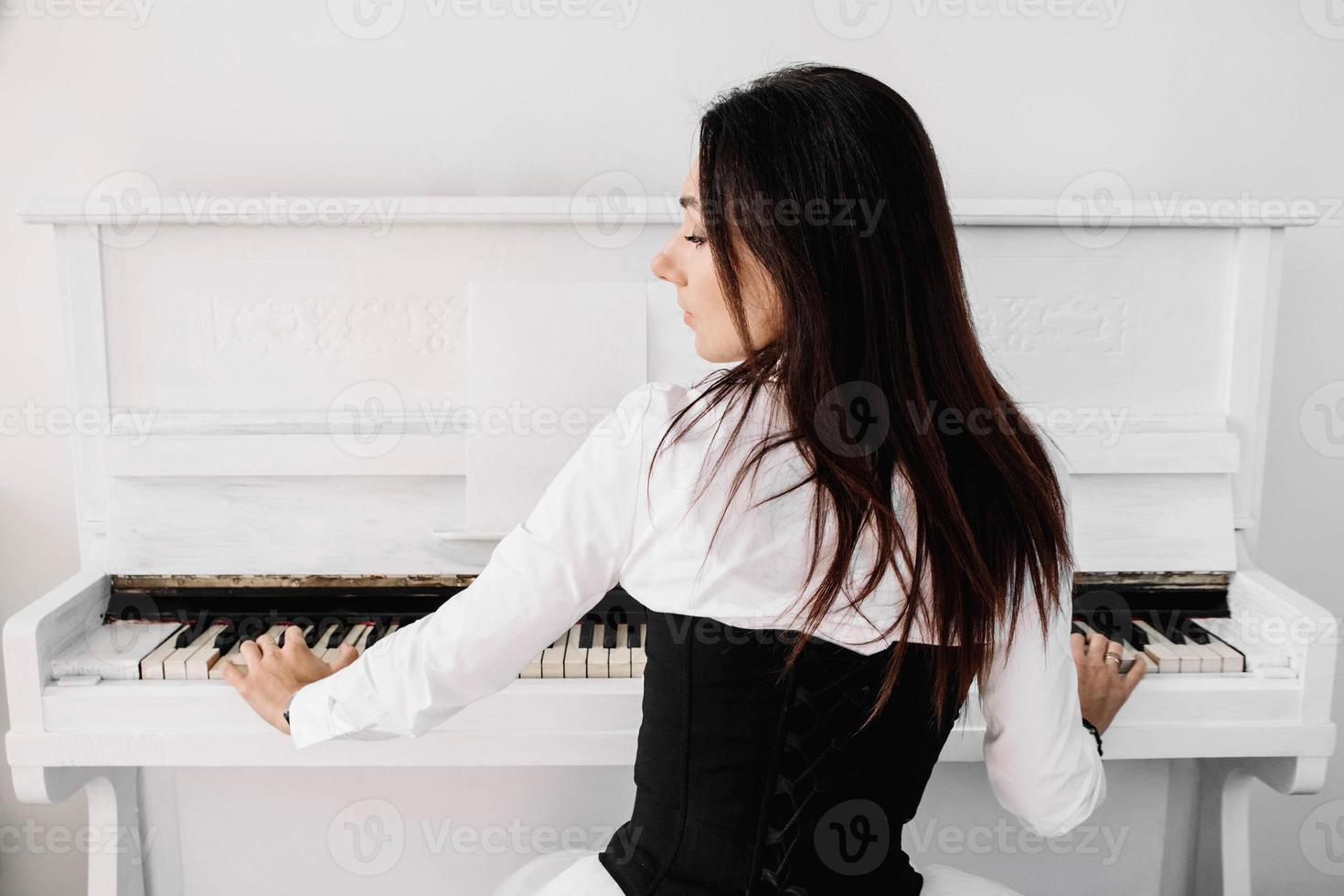 linda mulher vestida de vestido branco tocando piano branco foto