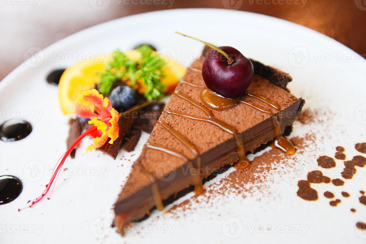 Bolo De Chocolate Caramelo Com Cereja E Frutas No Prato Branco - Close Up Da Fatia Do Bolo foto