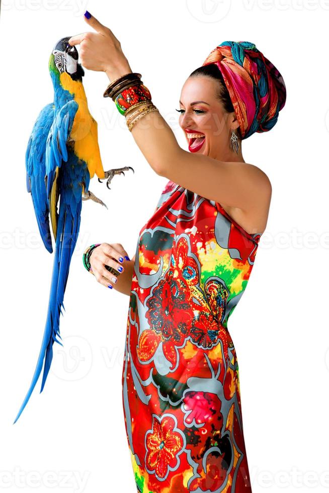 retrato de uma jovem mulher atraente rindo em estilo africano com um papagaio ara no dedo sobre fundo colorido foto
