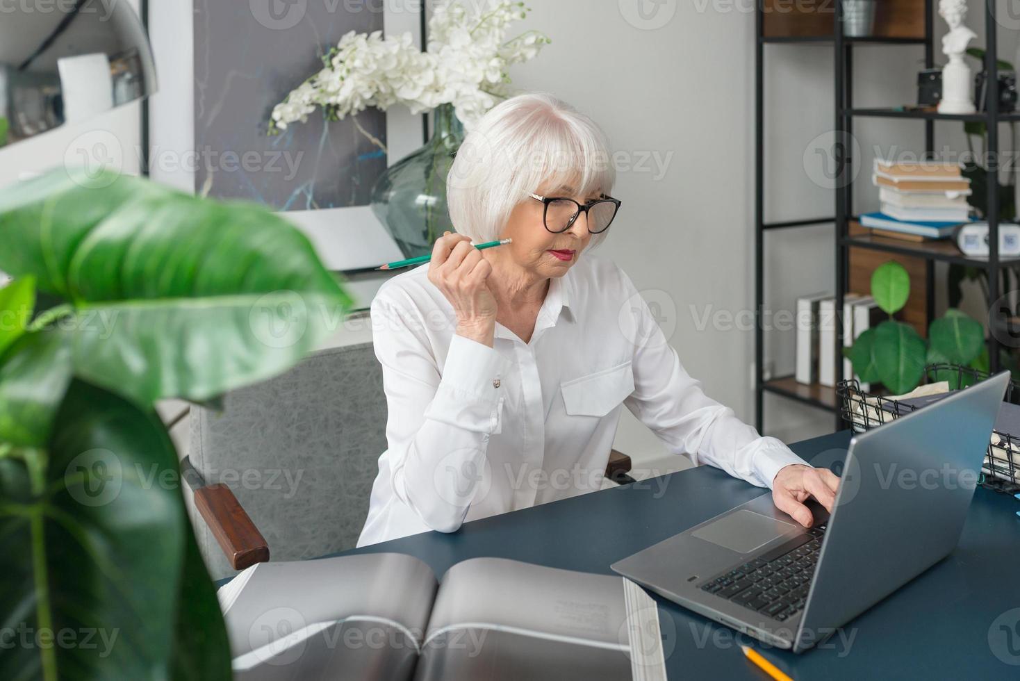 cansado sênior linda mulher de cabelo grisalho na blusa branca, lendo documentos no escritório. trabalho, pessoas seniores, problemas, encontrar uma solução, conceito de experiência foto