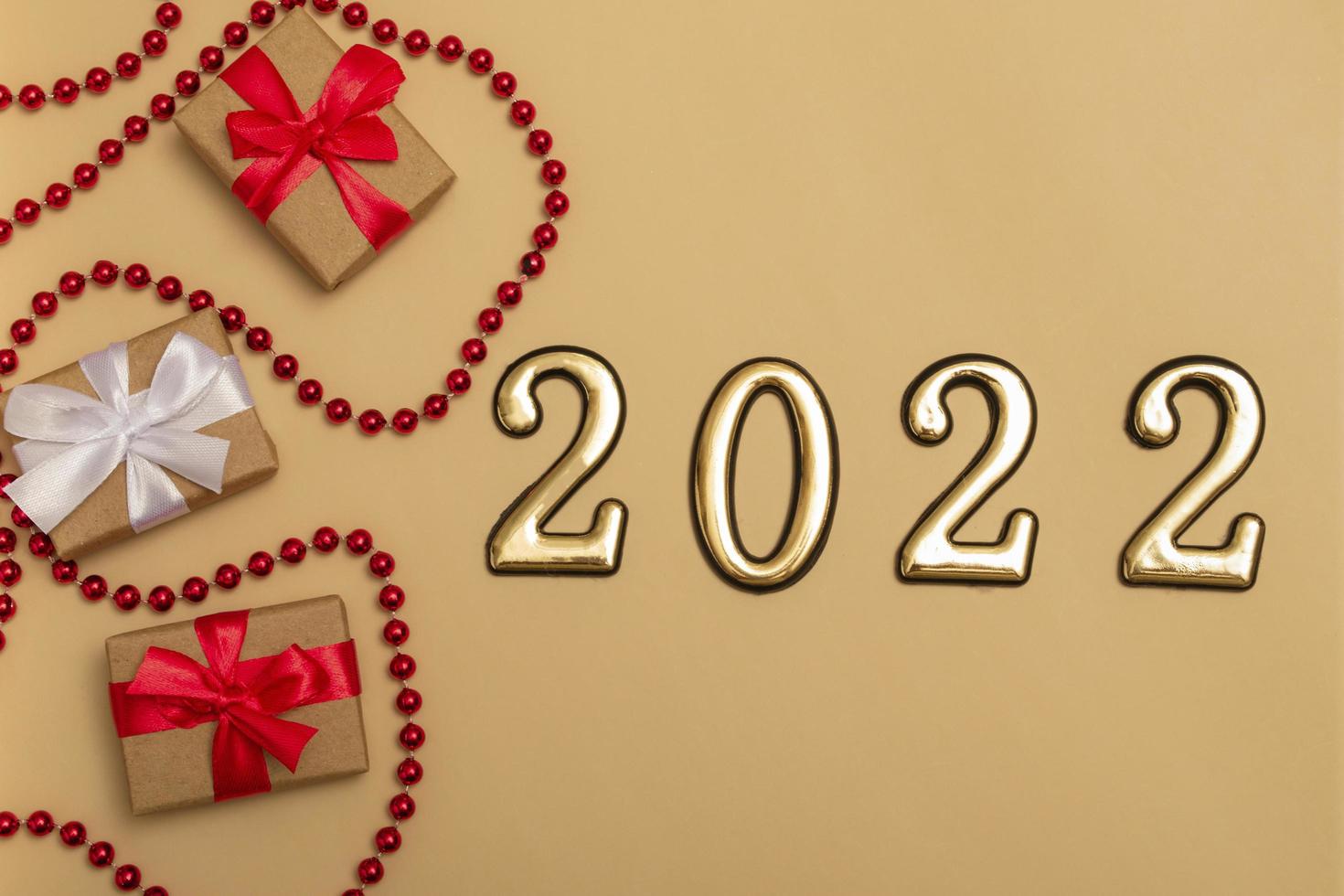 ano novo 2022. vista superior maquete de ano novo em fita vermelha de fundo bege, caixa de presente, números dourados e brilhos multicoloridos. layout de cartões postais, convites. foto