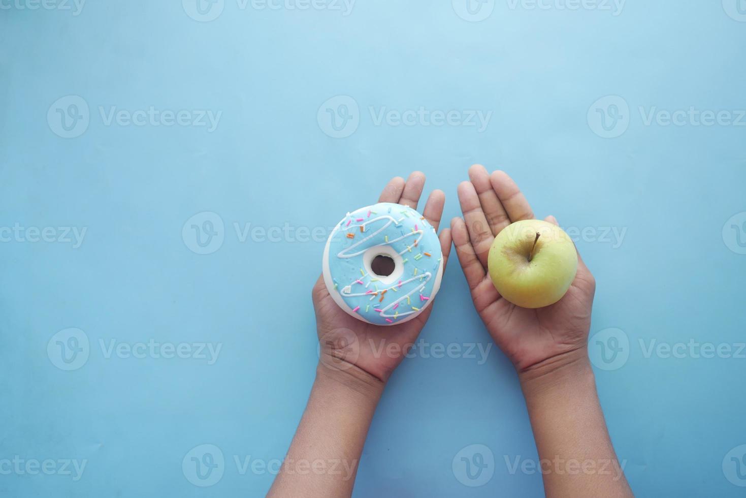 mão segurando rosquinhas e maçã disponível sobre fundo azul foto
