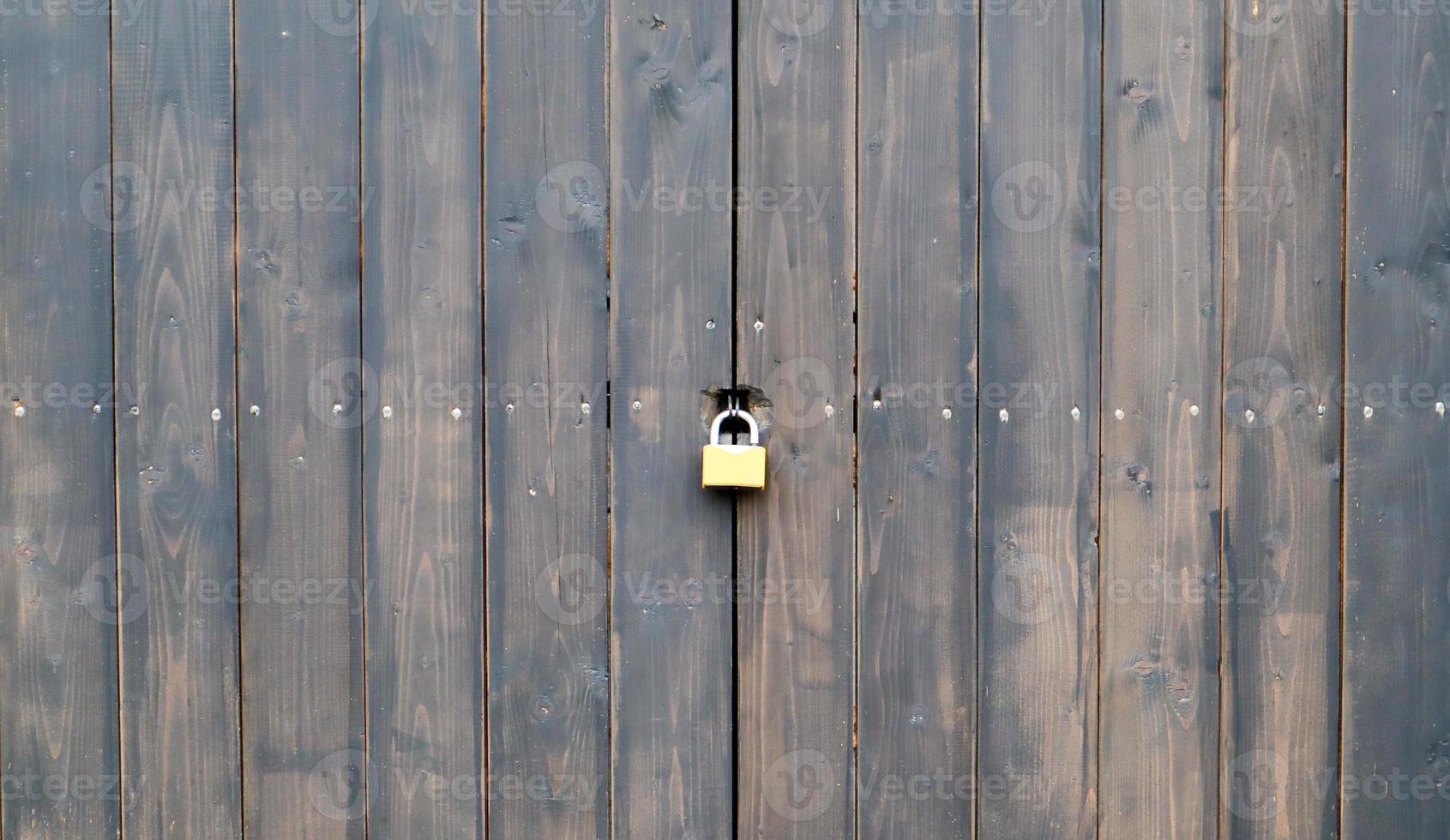 superfície de madeira de velhas pranchas marrons texturizadas fechadas em um cadeado enferrujado close-up. antigo portão de madeira com fechadura de metal. porta de madeira marrom com fechadura foto