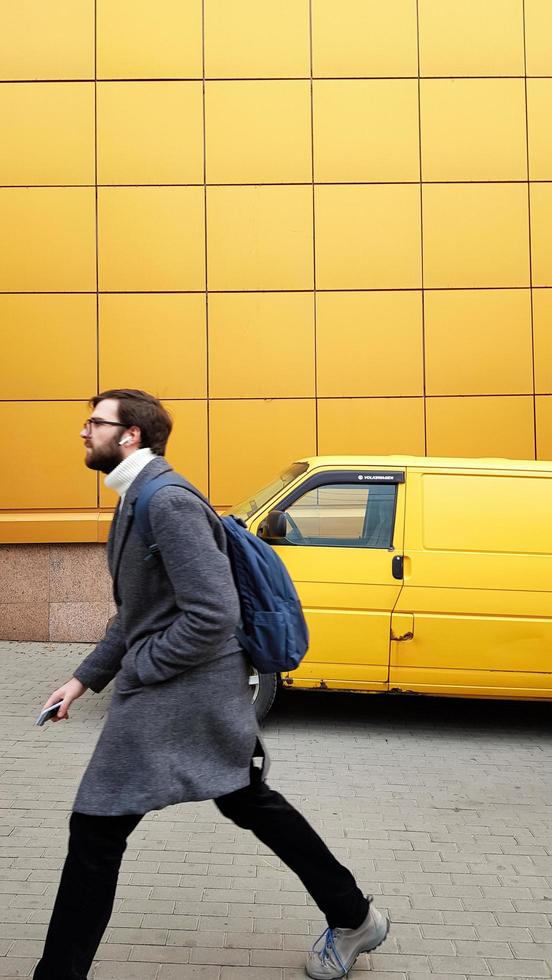 Ucrânia, kiev - 25 de fevereiro de 2020. um homem de negócios maduro com pressa para atender ou trabalhar com um casaco cinza sobre fundo amarelo. estilo casual. homem elegante com uma barba. modelo de moda masculina. foto