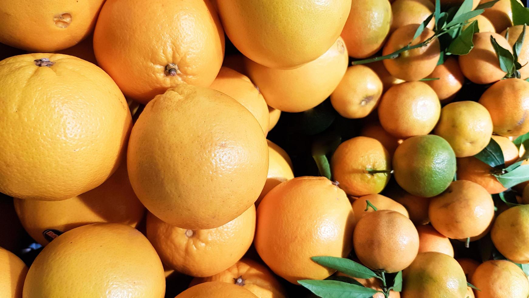 muita tangerina fresca amarela com folhas verdes no mercado, fundo de frutas. imagem de arte com folhas verdes. conceito de alimentação saudável. pode ser usado como um local para seu texto. foto