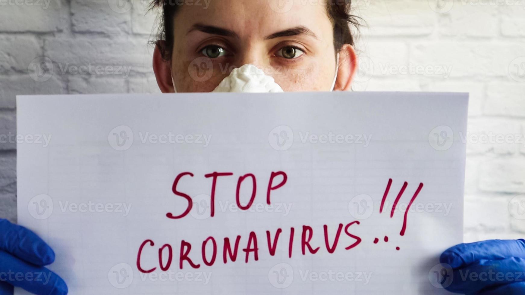 retrato de uma mulher com uma máscara protetora que mostra a câmera close-up folha de papel branca com o texto stop coronavirus escrito em marcador vermelho. o conceito de coronavírus quarentenário no mundo foto