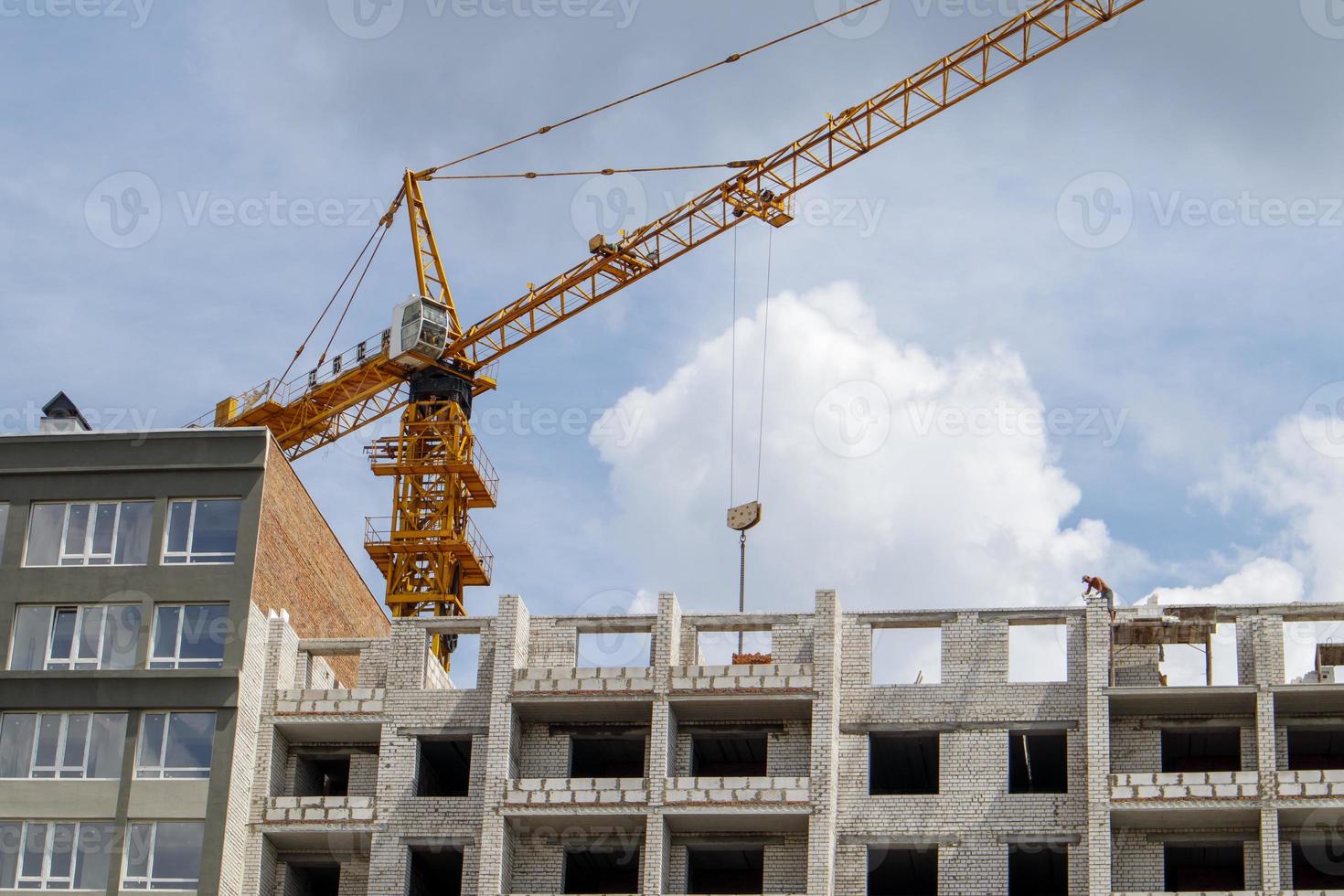 guindaste de construção em um edifício residencial inacabado contra o sol e o céu azul. construção de moradias, prédio de apartamentos na cidade. canteiro de obras de edifícios residenciais. foto