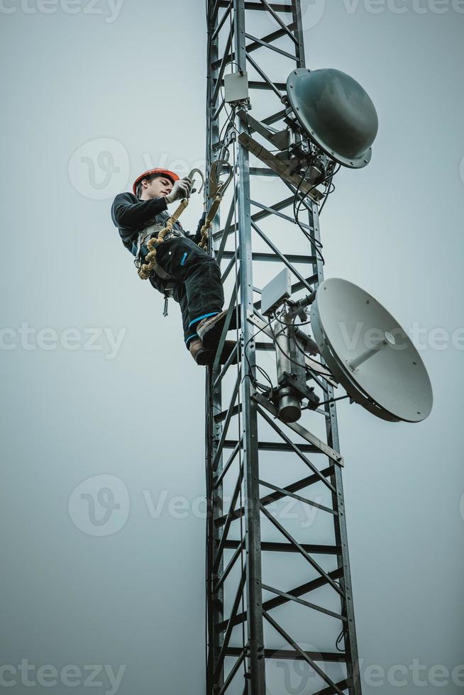 trabalhador de telecomunicações que prende o cinto de segurança do mosquetão foto