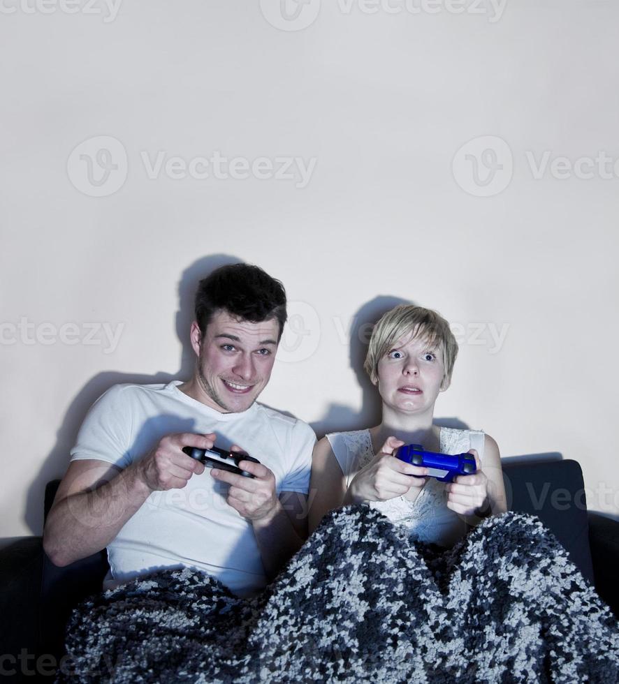 jovem casal jogando videogame confortavelmente embrulhado em um cobertor. foto