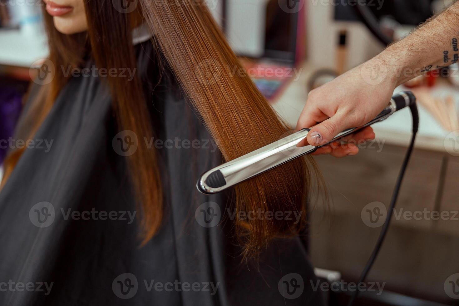 fechar-se do cabeleireiro mão segurando cabelo alisador e fazer Penteado para fêmea cliente foto