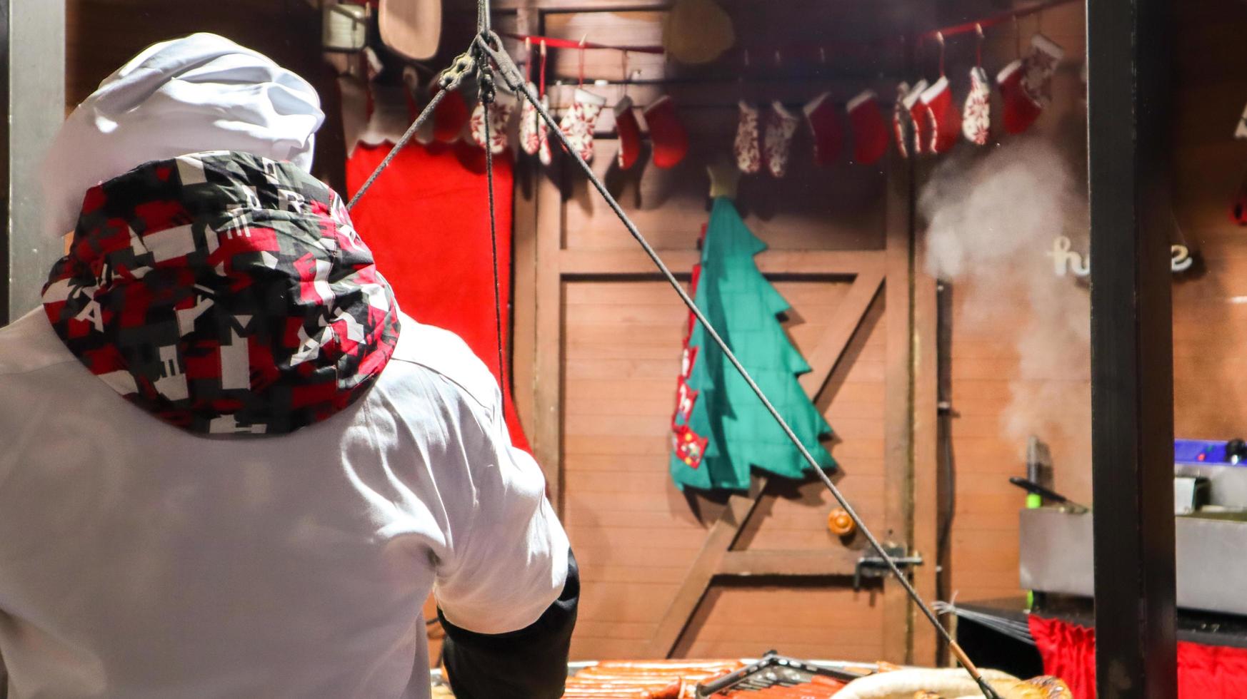 o chef prepara kebabs grelhados, comida de rua e banquetes culinários. salsicha fresca e grelha ao ar livre. um homem está preparando comida de rua da culinária alemã. mercado de natal na europa. feira da cidade do festival foto