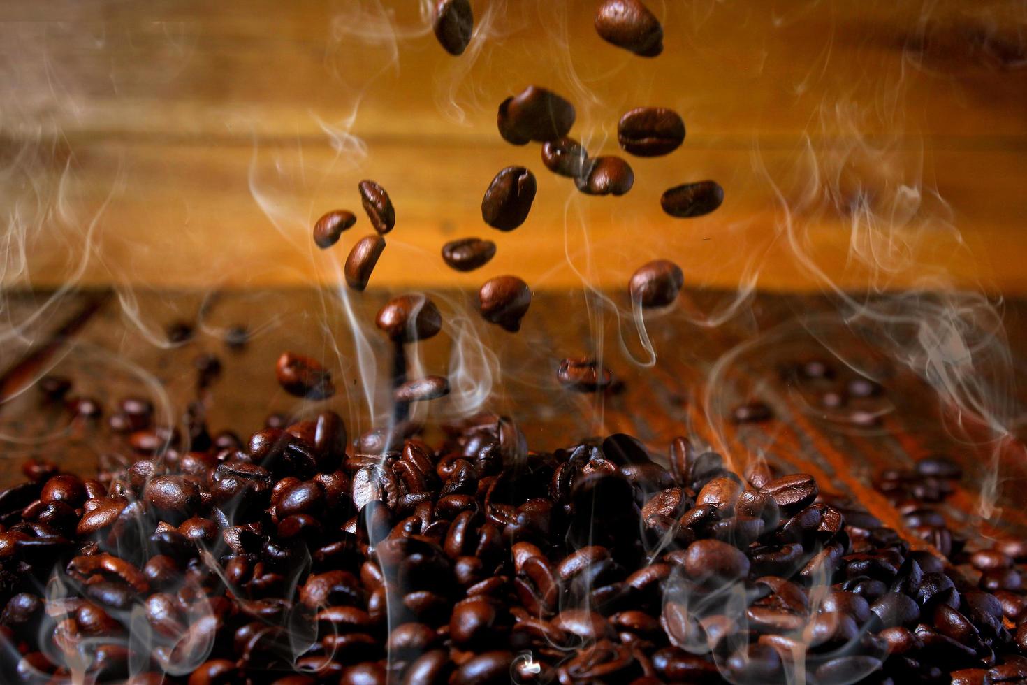 grãos de café torrados caindo na pilha, quentes e esfumaçados. fundo de madeira rústica desfocado foto