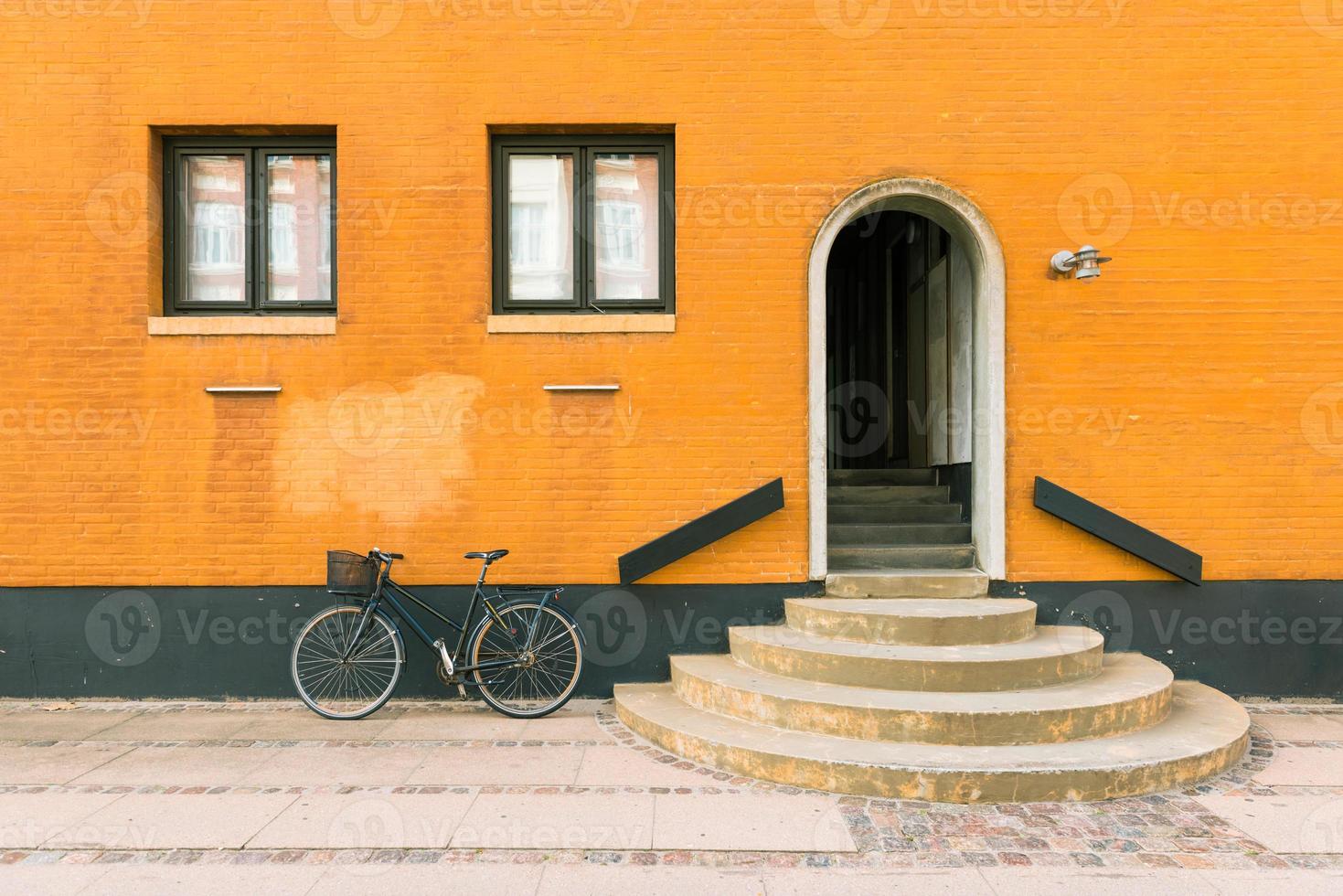 bicicleta preta perto da parede amarelo-laranja do antigo edifício residencial em copenhague, dinamarca foto