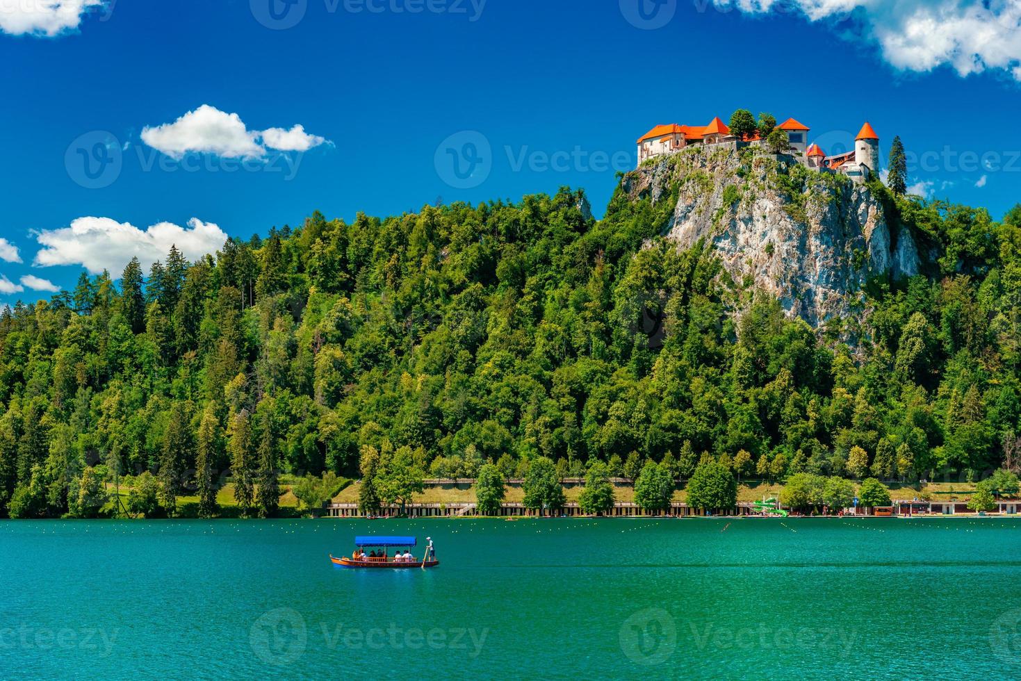 o lago sangrou na Eslovênia. paisagem pitoresca de verão com um castelo em uma colina coberta por uma floresta verde, um barco com turistas e um lago de águas azul-turquesa foto