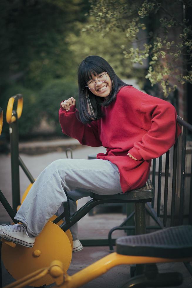 adolescente asiático rindo com cara de riso sentado no equipamento de ginástica do parque foto