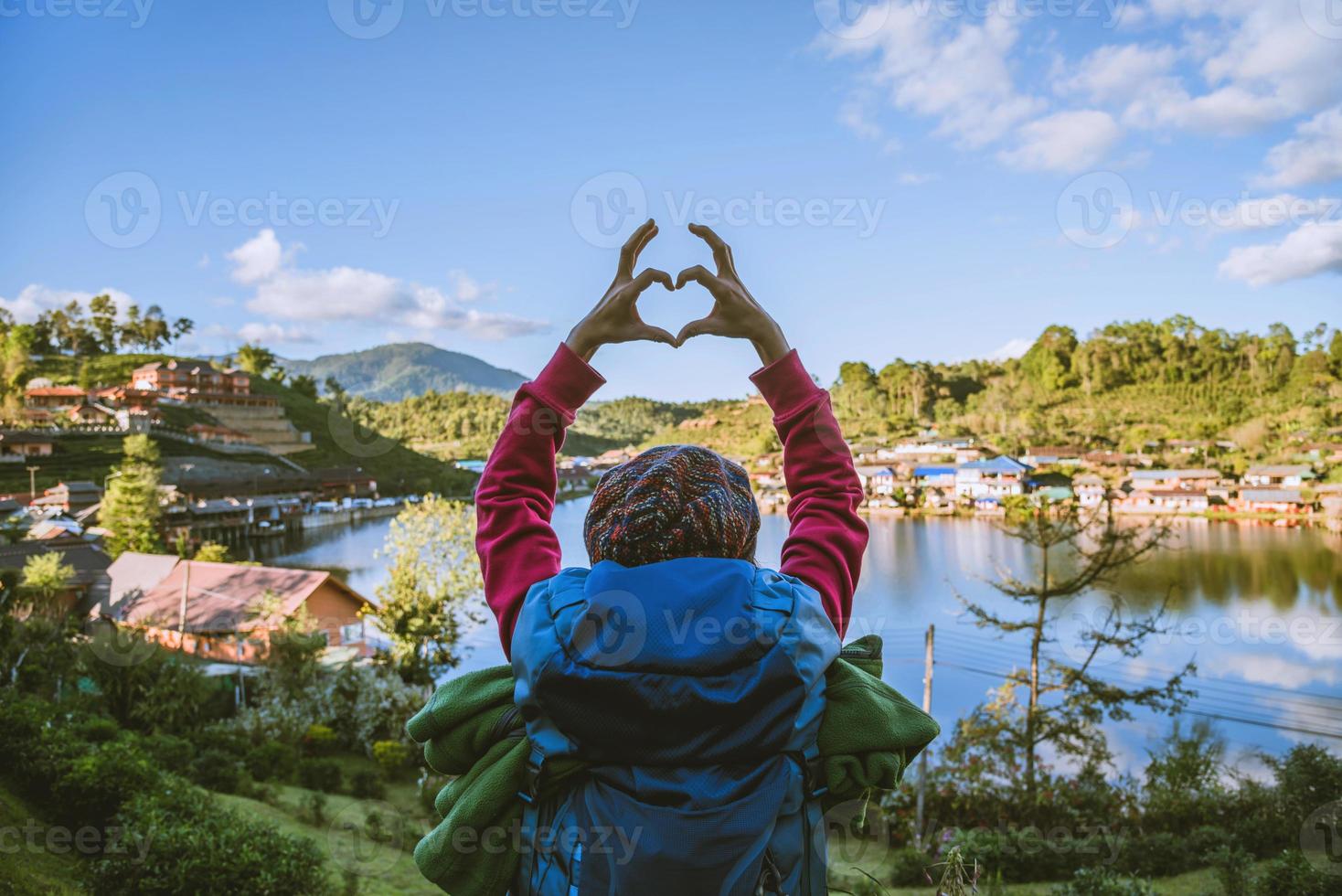 uma garota com uma mochila, desfrutando de uma viagem em uma montanha na zona rural. garota feliz com turismo relaxante, ela levantou a mão para fazer um formato de coração. foto