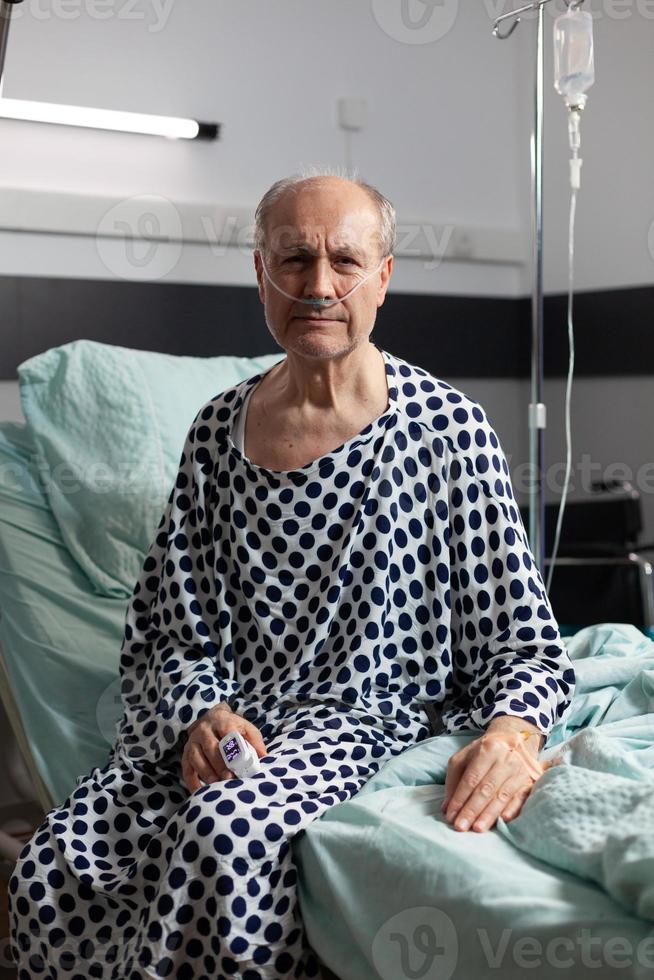 retrato de homem idoso triste e indisposto, sentado na beira de uma cama de hospital foto