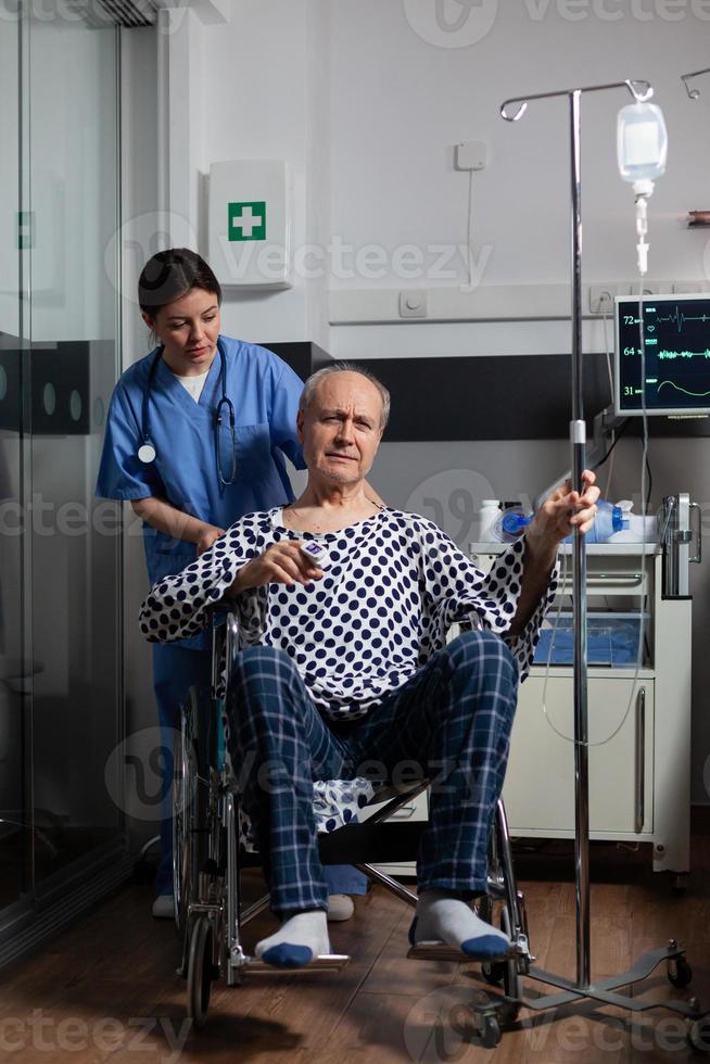 homem idoso hospitalizado sentado em uma cadeira de rodas em um quarto de hospital foto