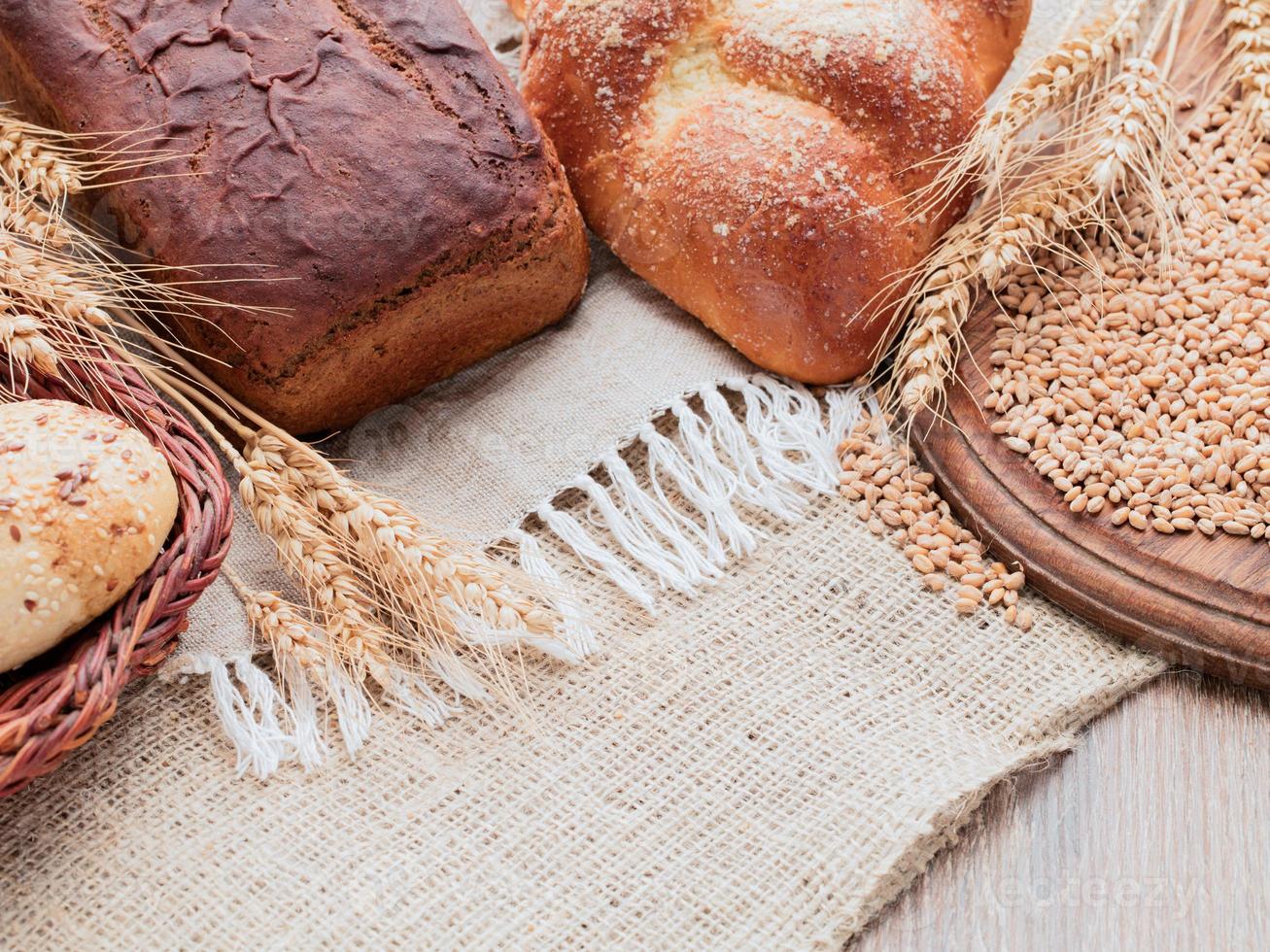 espiguetas de centeio, pão de trigo, pão na cesta. lona, estopa, mesa de madeira, tábua de madeira. foto