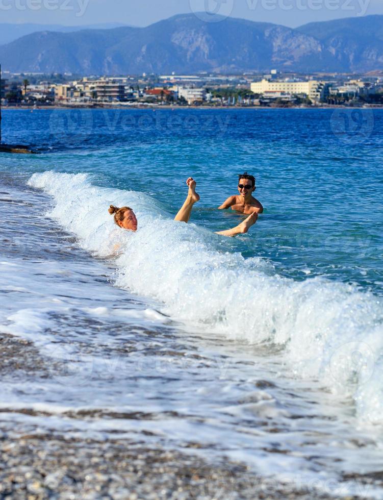 uma onda costeira derruba uma jovem que entra no mar por uma praia de seixos. foto