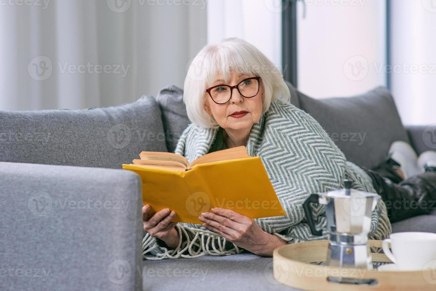 mulher sênior antiquada deitada no sofá lendo um livro. educação, maduro, conceito de lazer foto