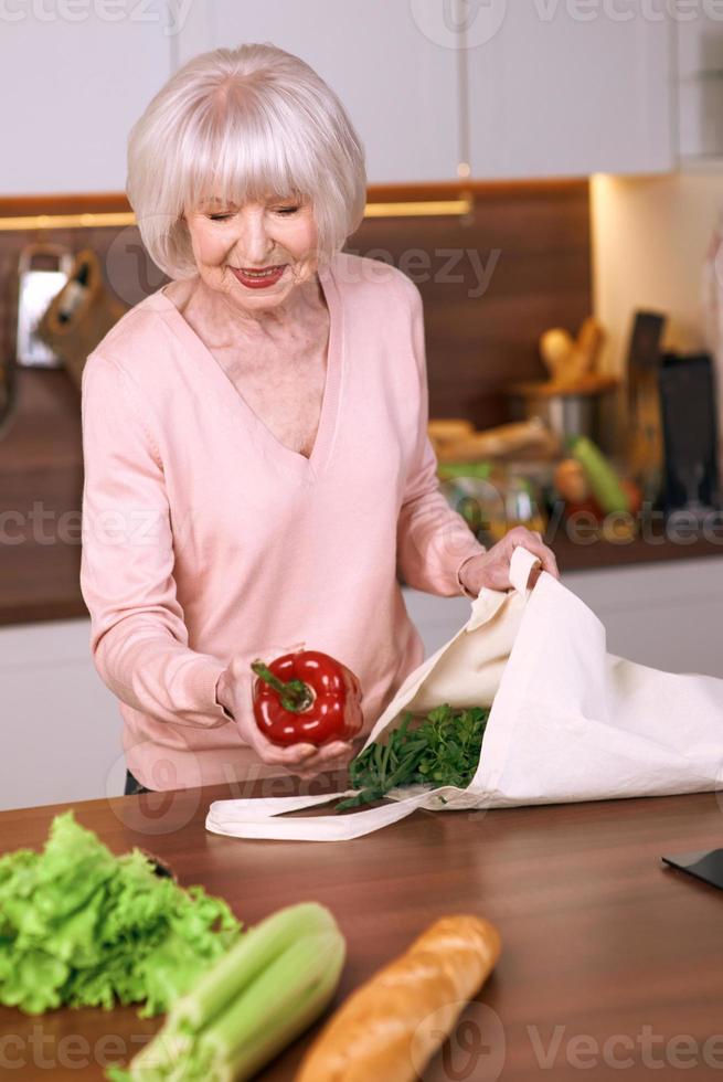 mulher alegre sênior é reembalagem de supermercado na cozinha moderna. alimentos, habilidades, conceito de estilo de vida foto