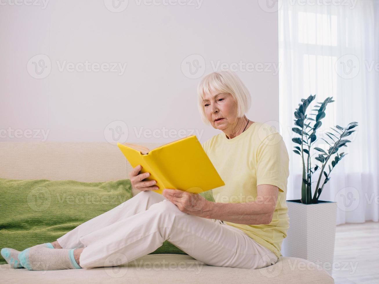 mulher sênior com cabelos grisalhos, lendo um livro no sofá em casa. educação, pensão, anti-idade, conceito de leitura foto
