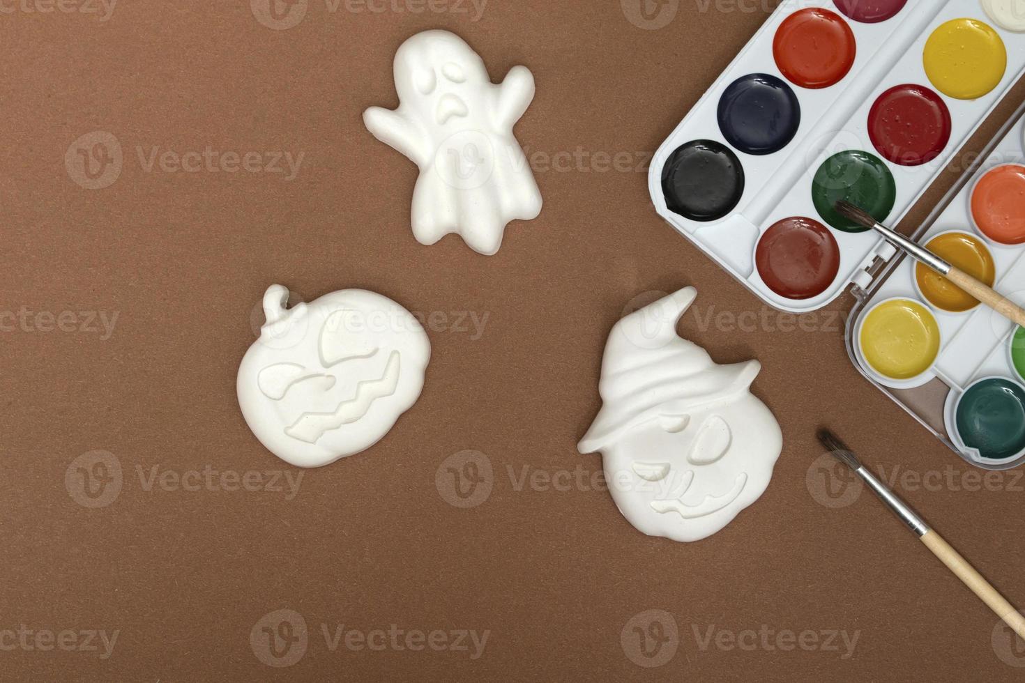 artesanato de halloween. estatuetas de abóboras e fantasmas em tinta brilhante com um pincel em um fundo marrom, prontas para serem desenhadas em close-up foto