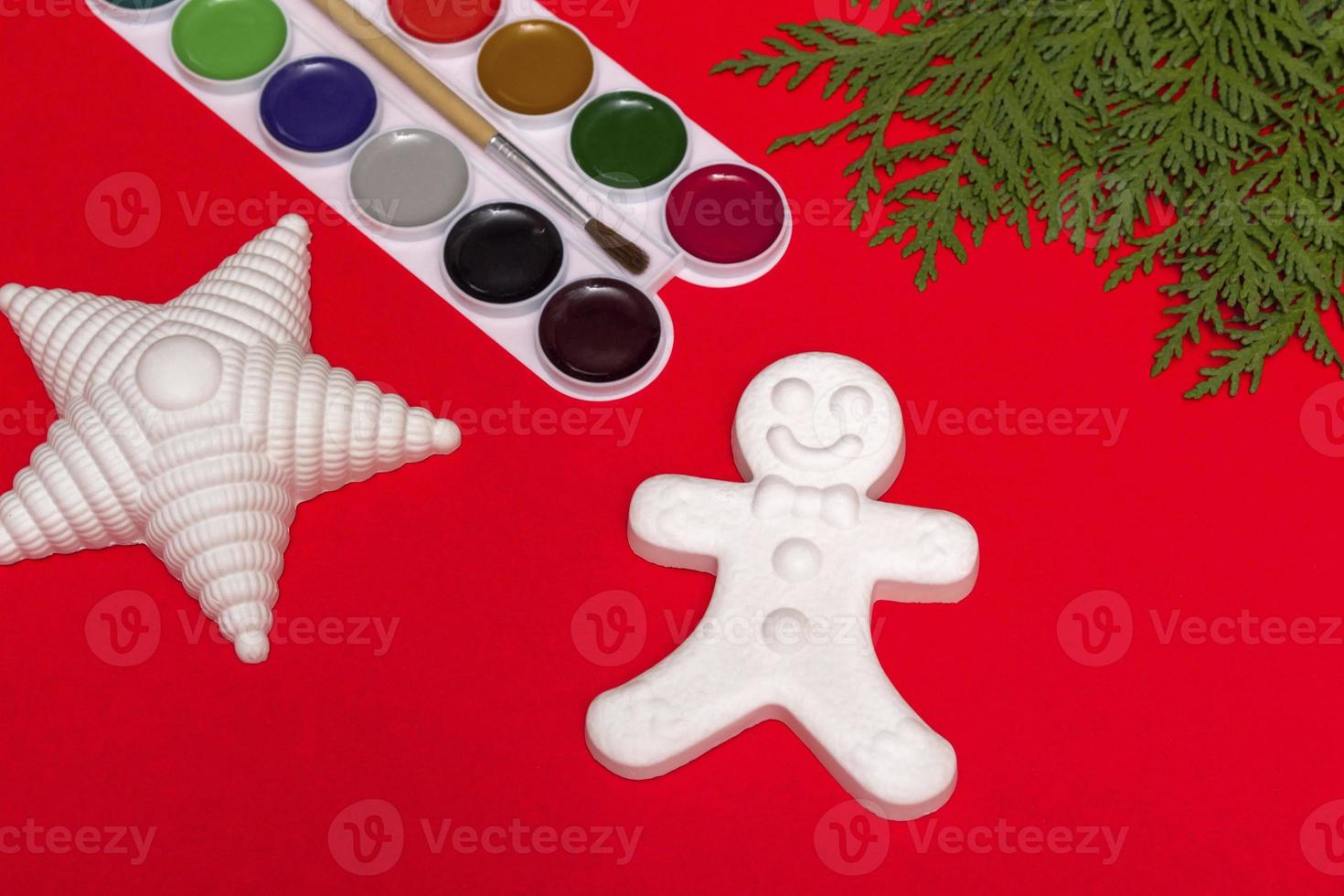 Natal decorativo gingerbread man, estrela e tintas, conceito de criatividade em um fundo vermelho com um galho de uma árvore de Natal. com espaço de cópia foto