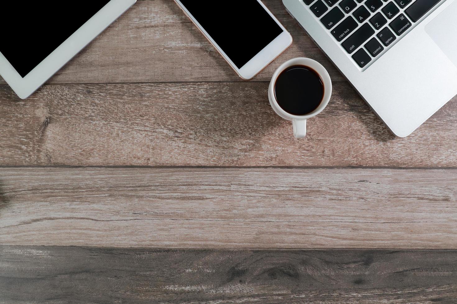 mesa de escritório de madeira com computador, tablet e smartphone com xícara de café foto