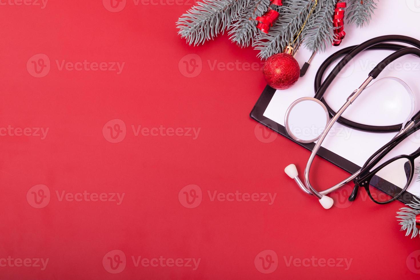 área de transferência com estetoscópio médico, óculos, árvore de Natal em fundo vermelho com espaço de cópia foto