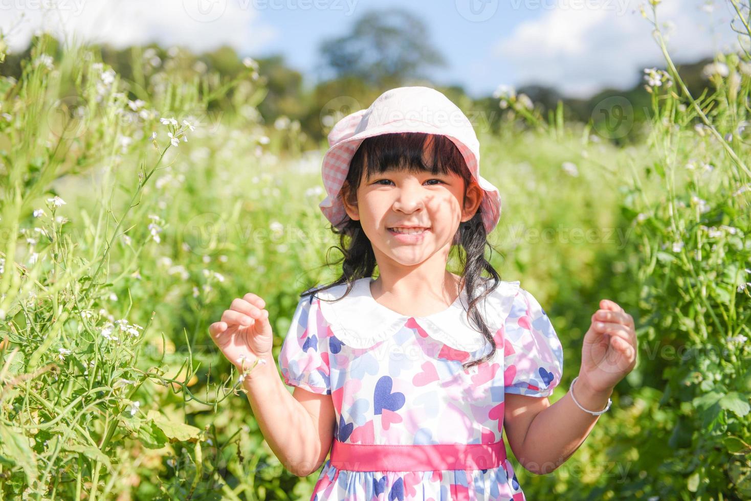 menina criança asiática se divertir com um rosto feliz e sorridente na flor natural do jardim da manhã foto