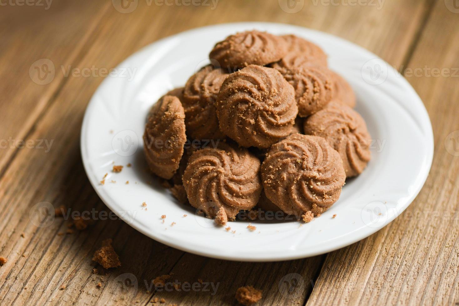 biscoitos de chocolate na chapa branca e fundo de madeira, mini biscoitos biscoitos. foto