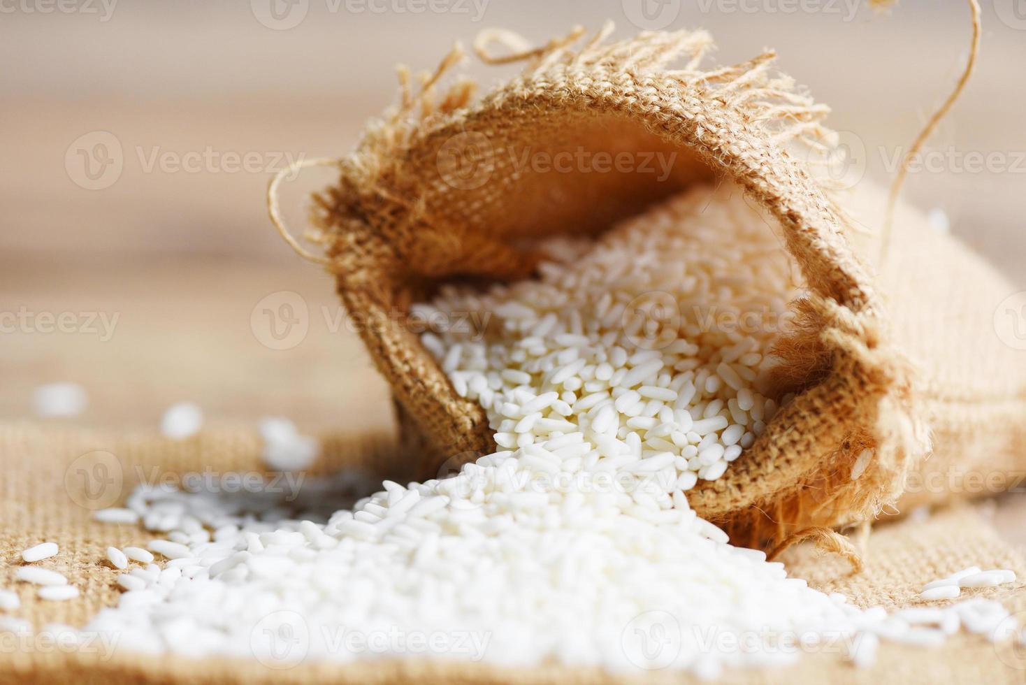 arroz branco de jasmim no saco e arroz colhido na mesa de madeira, conceito de cozimento de grãos de arroz e alimentos foto