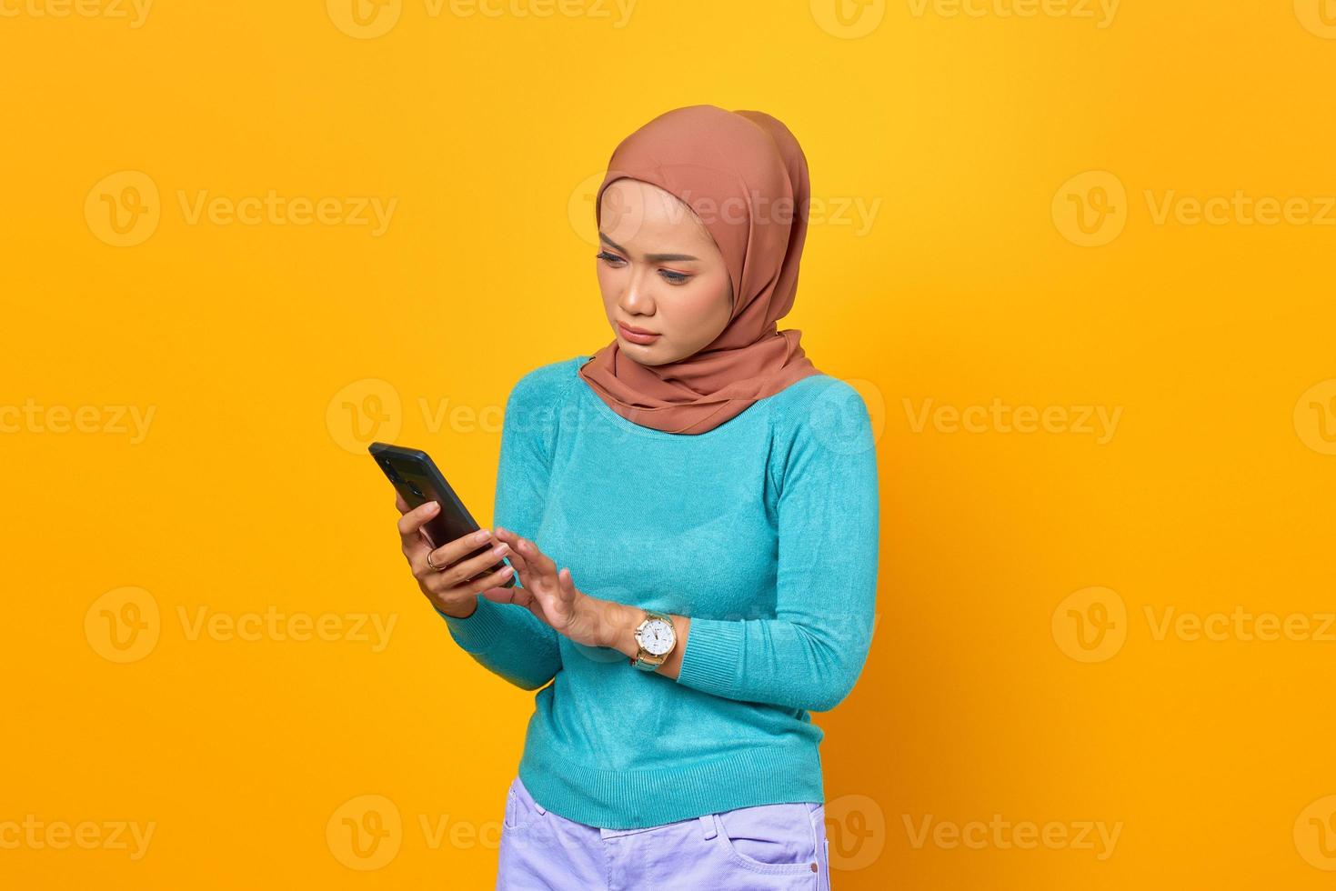 Mulher jovem e bonita asiática triste usando smartphone isolado em fundo amarelo foto