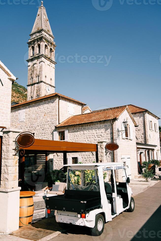 pequeno golfe carrinho carrinhos lado de fora uma restaurante perto a velho pedra construção negligenciar a Igreja Sino torre foto