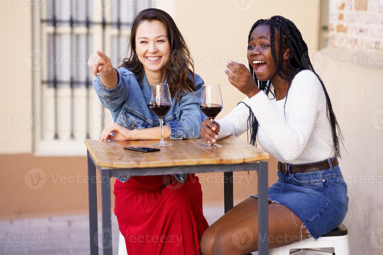 duas mulheres bebendo vinho tinto, sentadas à mesa do lado de fora de um bar. foto