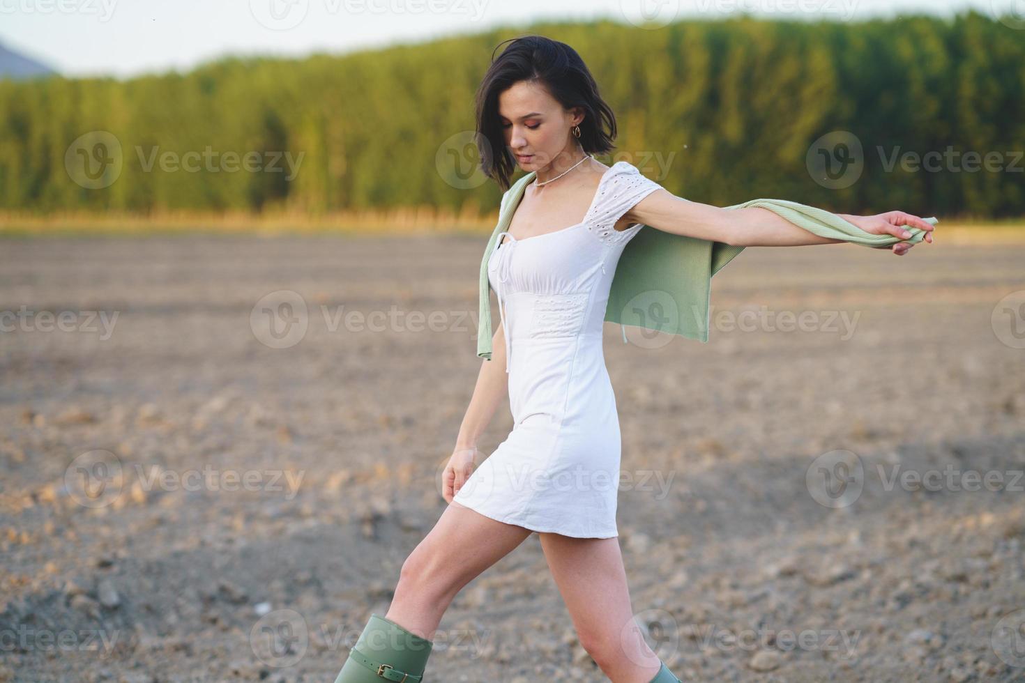 mulher asiática, caminhando na zona rural, usando um vestido branco e galochas verdes. foto