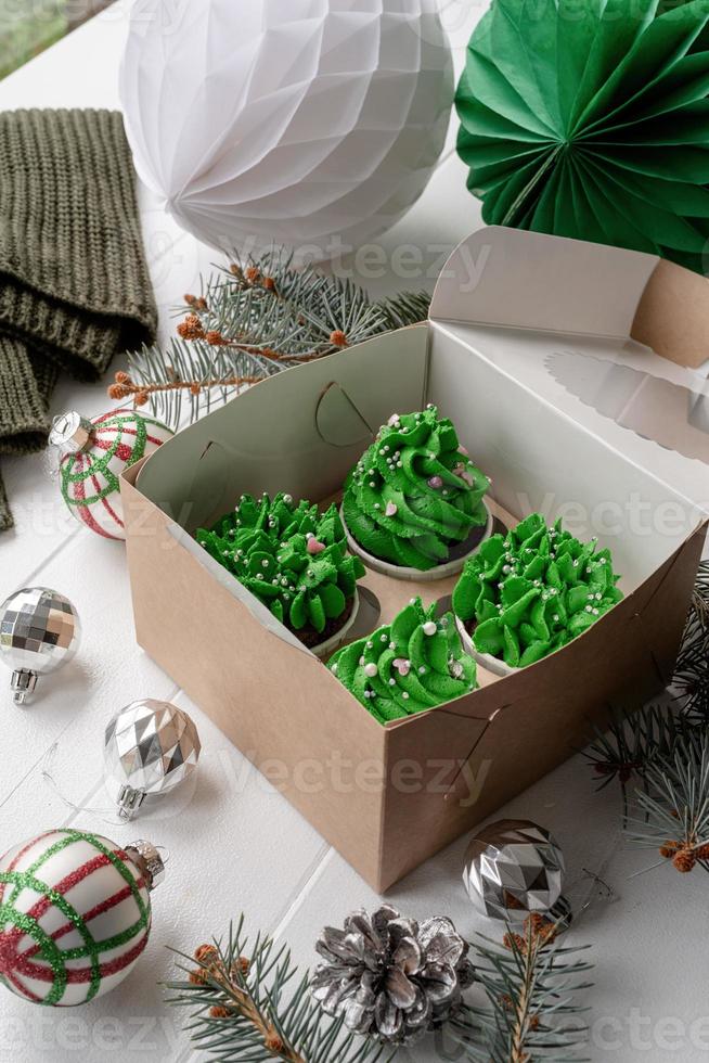Cupcakes em forma de árvore de Natal em caixa ecológica artesanal, cercados de decorações festivas foto
